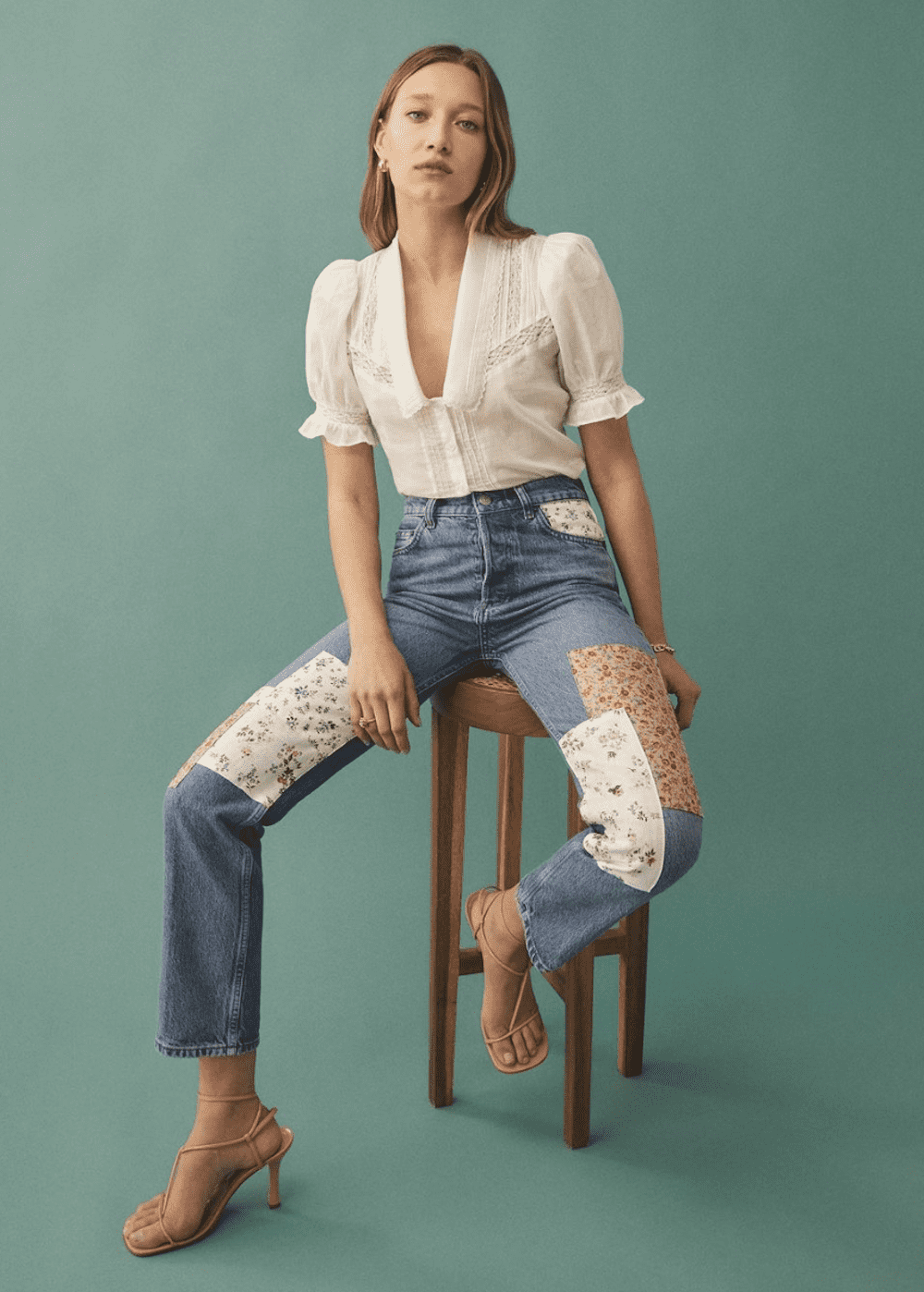 image of a woman sitting on a stool wearing floral patch jeans and a white embroidered blouse