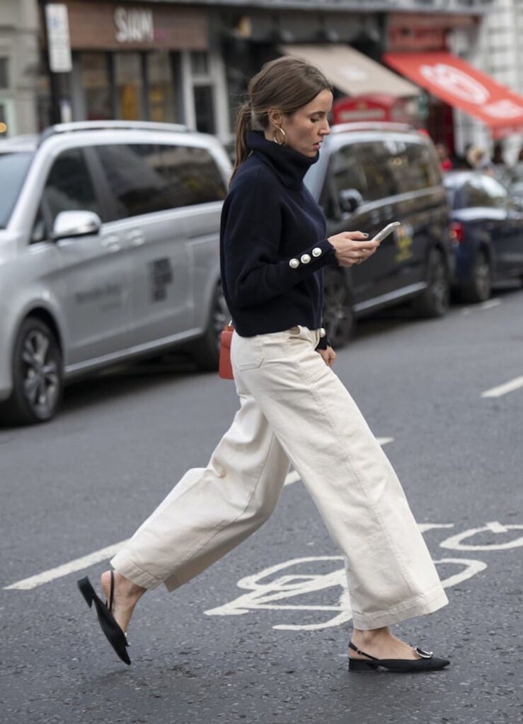 image of a woman crossing the street wearing white wide leg jeans and a turtleneck sweater