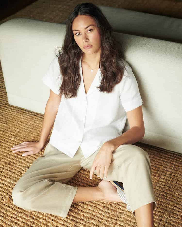 image of a woman sitting on a jute carpet against a white couch wearing a white linen shirt and beige pants 