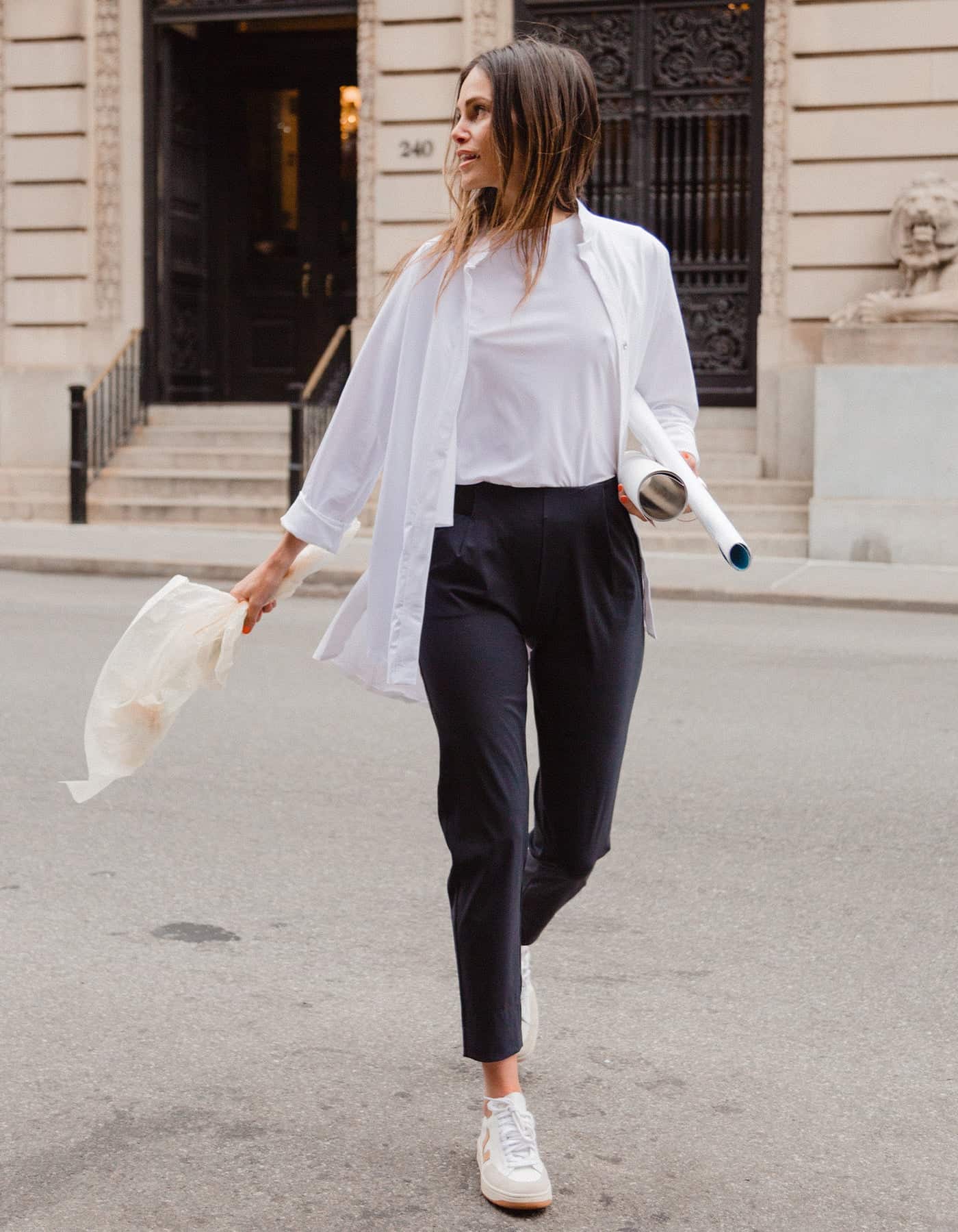 image of a woman crossing the street in a white t-shirt, white button up, navy pants, and sneakers