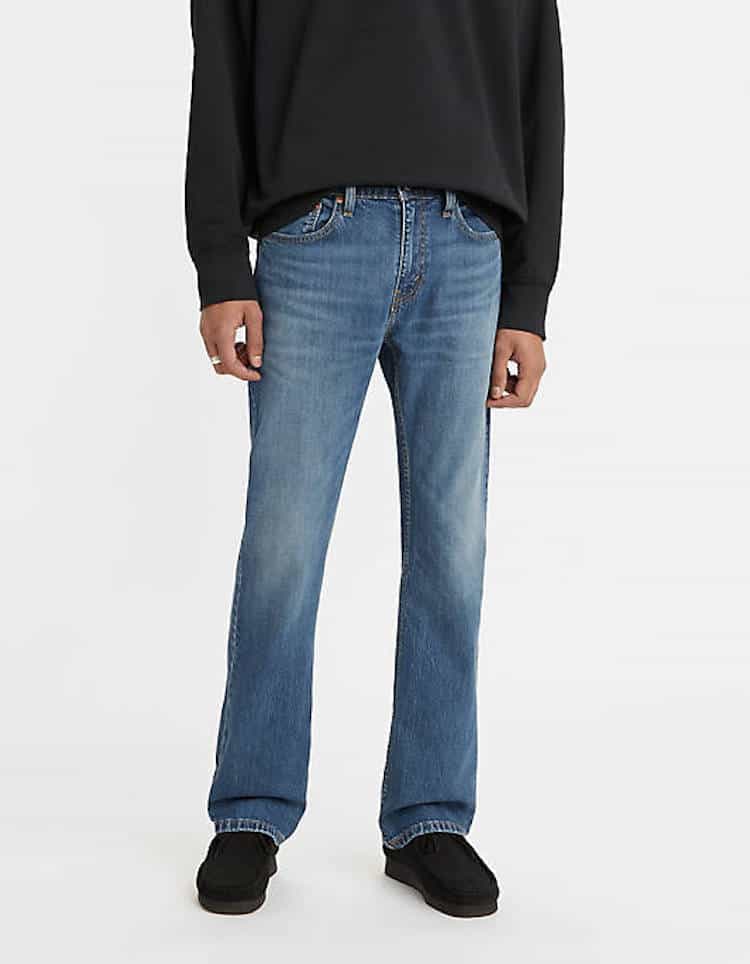 image of a man from the waist down wearing a black sweater, blue bootcut jeans, and black shoes