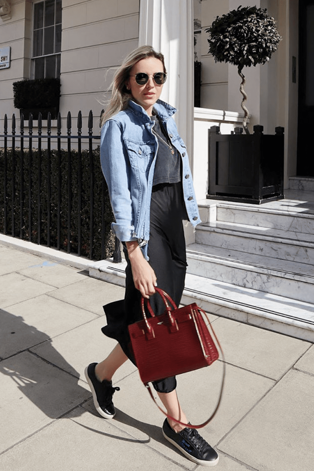 image of a woman wearing a blue jean jacket and black dress with a red purse and sneakers