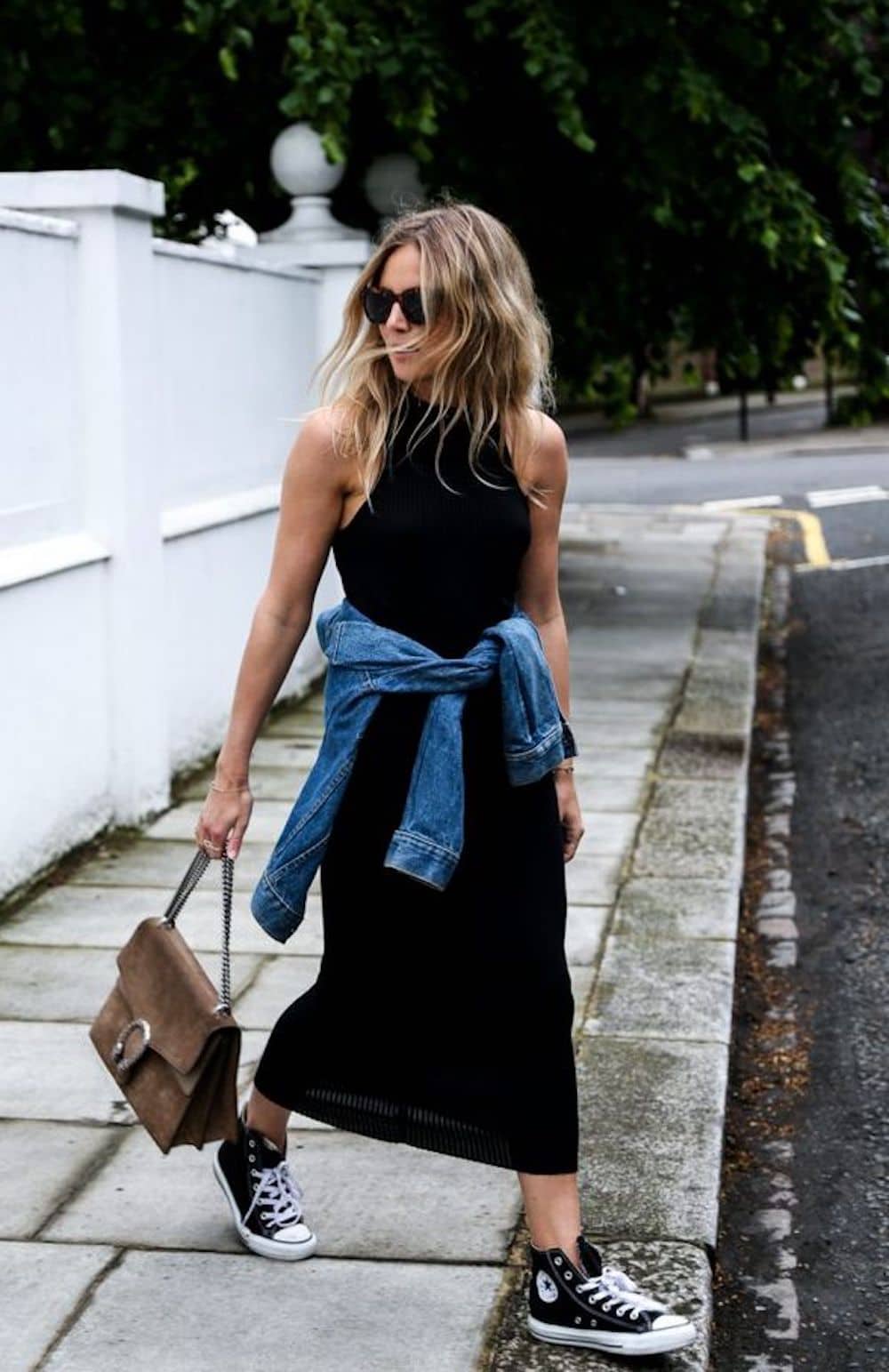 image of a woman crossing the street wearing a black dress and sneakers with a jean jacket tied around her waist