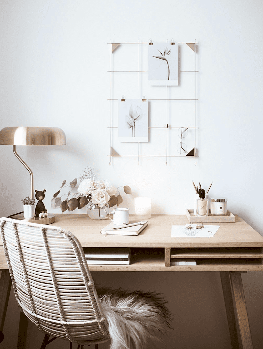 image of a wooden desk in front of a white wall with neutral, minimal decor and a rattan chair and gold lamp