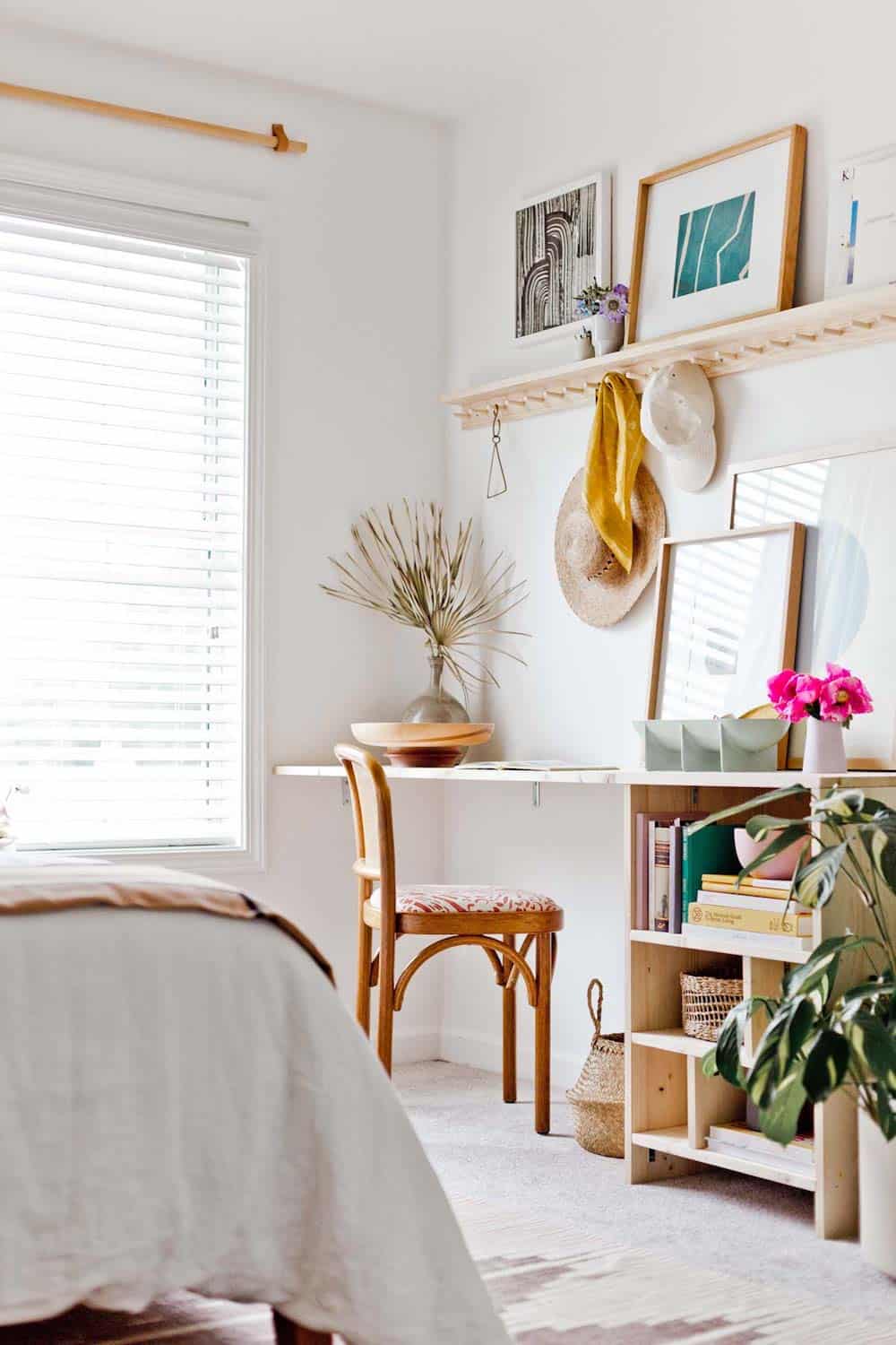 image of a desk in a bedroom with white walls and a minimal gallery of art and some plants