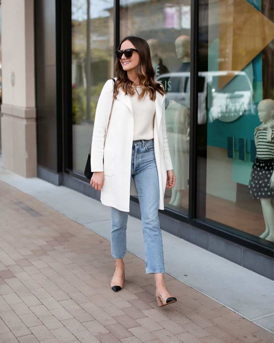 image of a woman walking down a sidewalk wearing a long white jacket, mom jeans, and heels