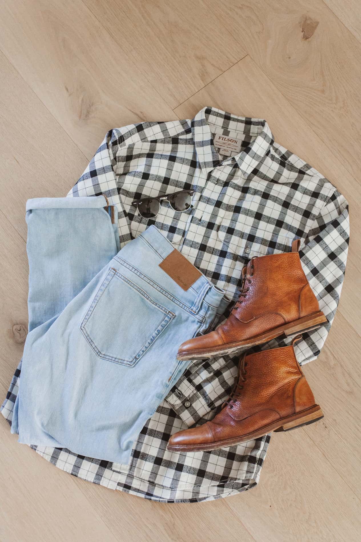 image of an outfit flat lay with a plaid white and black flannel button up shirt, brown boots, and light blue jeans