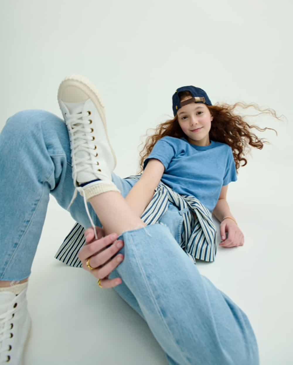 image of a young girl in a blue t-shirt and jeans leaning back with her foot up on her knee