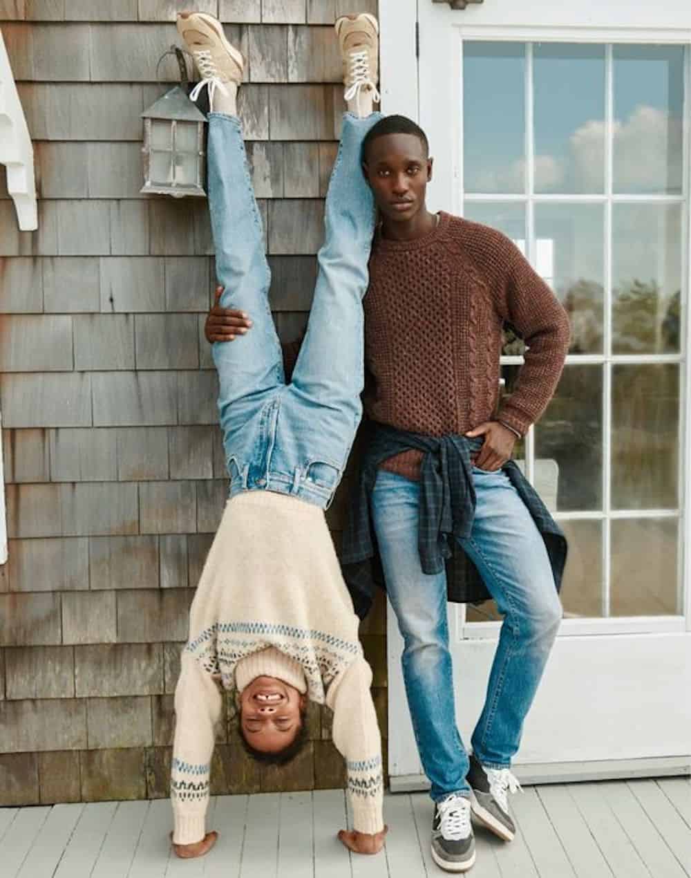 image of a black man and black woman standing in front of a house in jeans and sweaters and the woman is doing a handstand and smiling