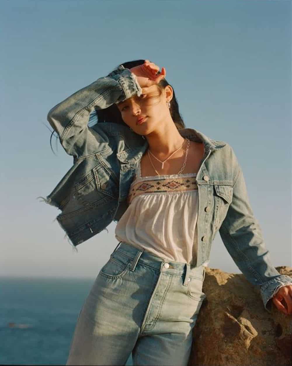 image of a teenage girl wearing a jean jacket, white top, and jeans standing in front of the ocean