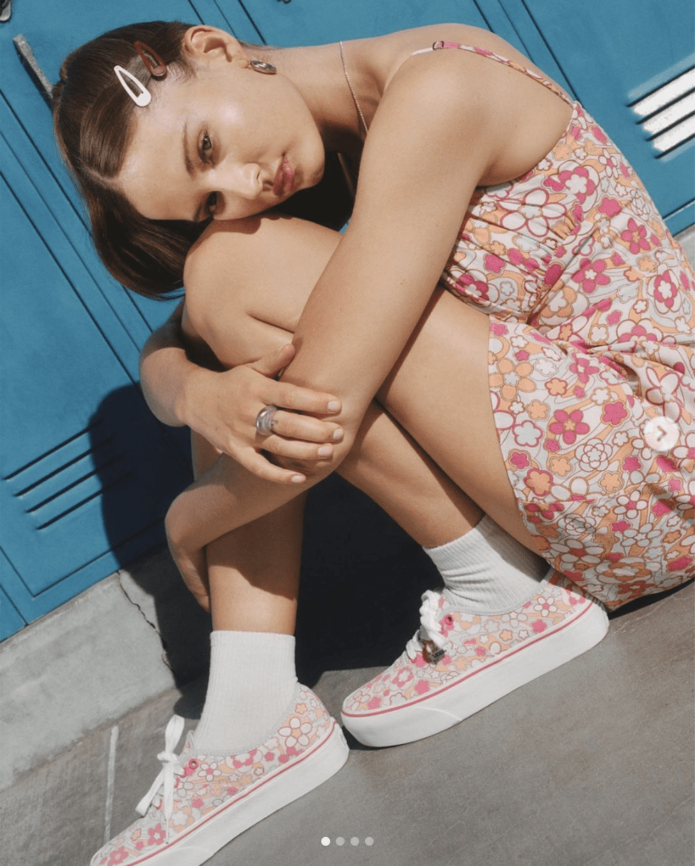 image of a teenage girl wearing a floral dress and matching floral pattern shoes sitting crouched in front of blue lockers