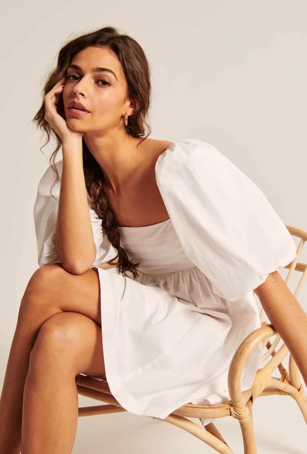 image of a brunette woman sitting in a cane chair with a white puff-sleeve dress on