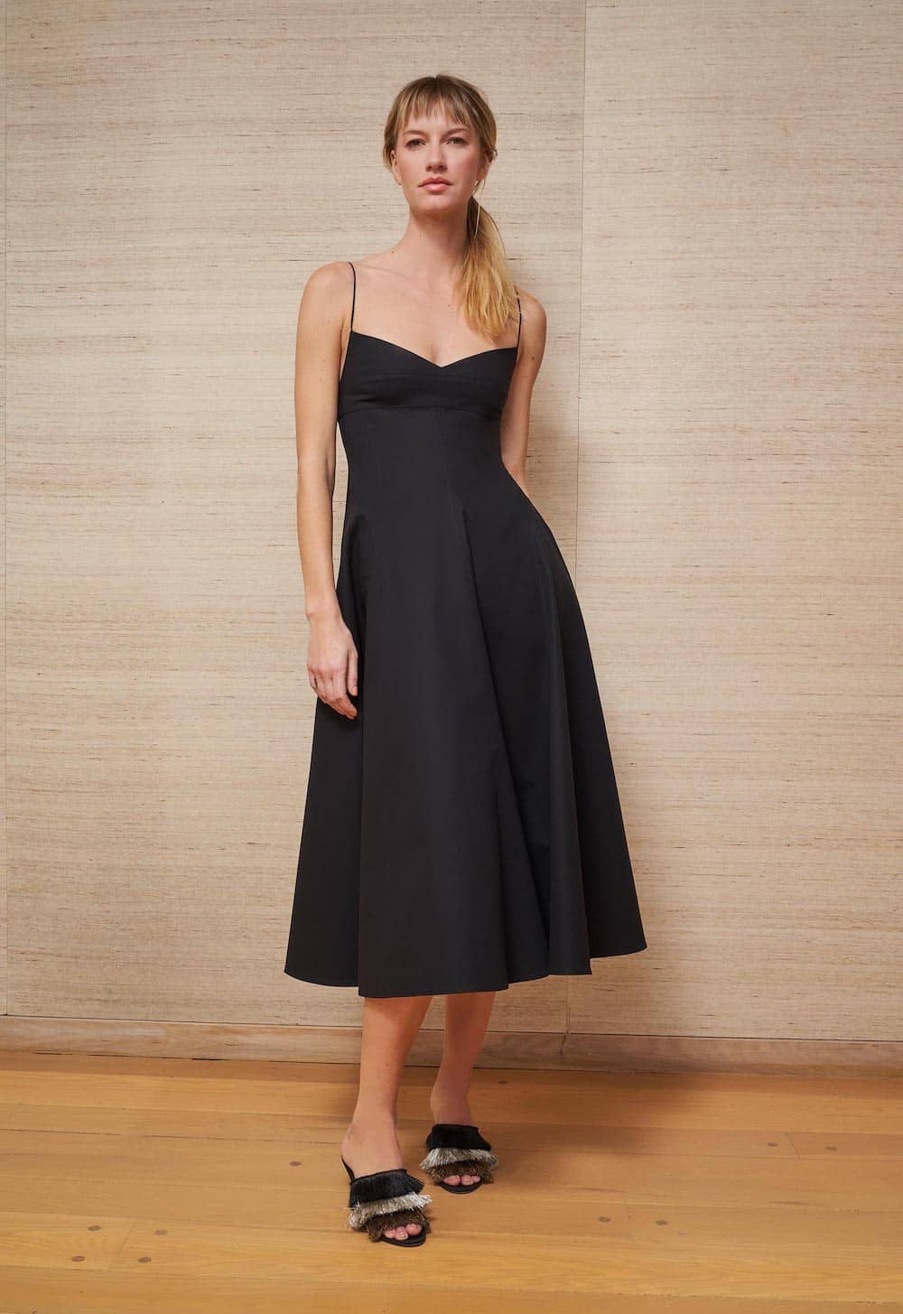 image of a woman standing against a neutral wall wearing a black a-line midi dress
