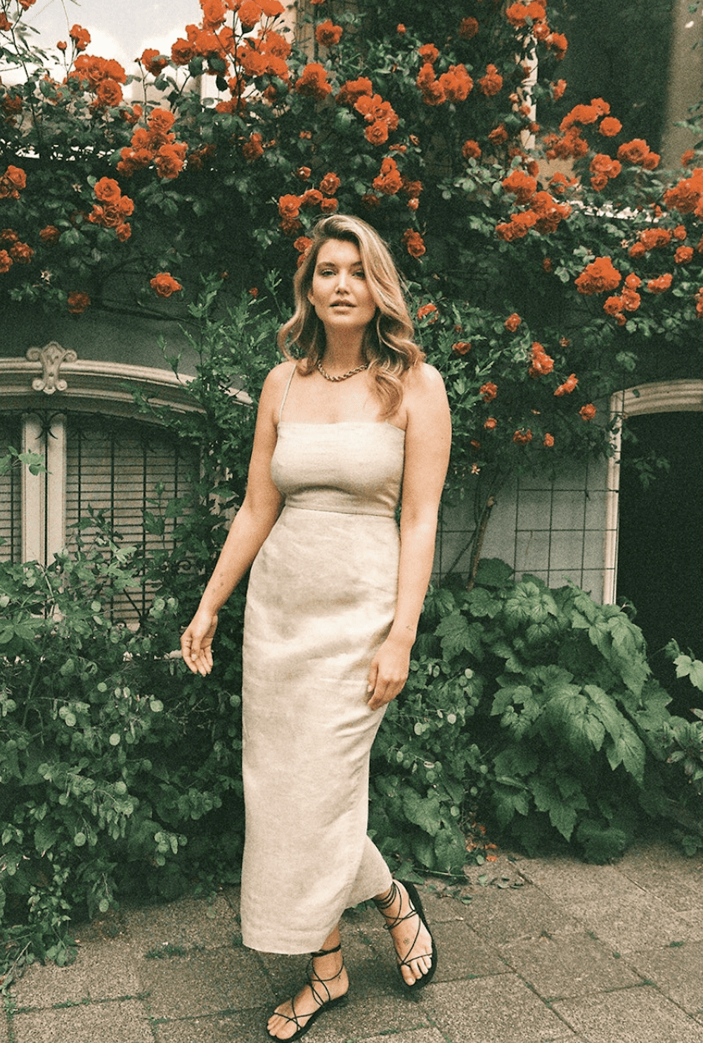 image of a woman in a long beige linen dress standing in front of flowers