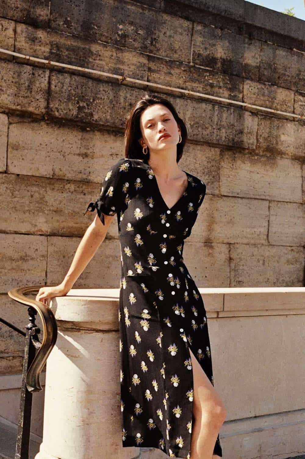 image of a woman leaning against a stair railing wearing a black floral midi dress