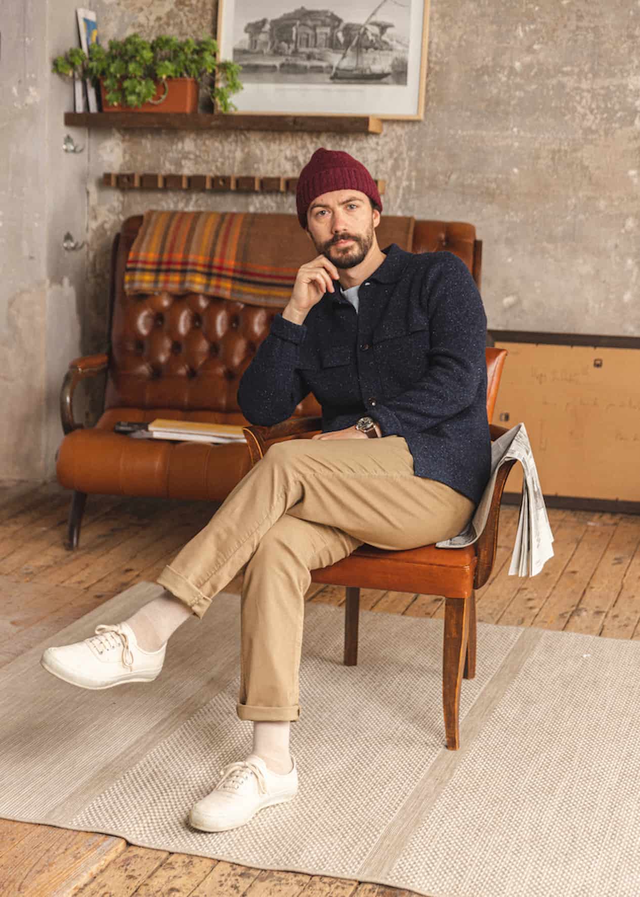 image of a man sitting in a chair wearing khaki pants, white sneakers, a navy blue flannel shirt and a red toque