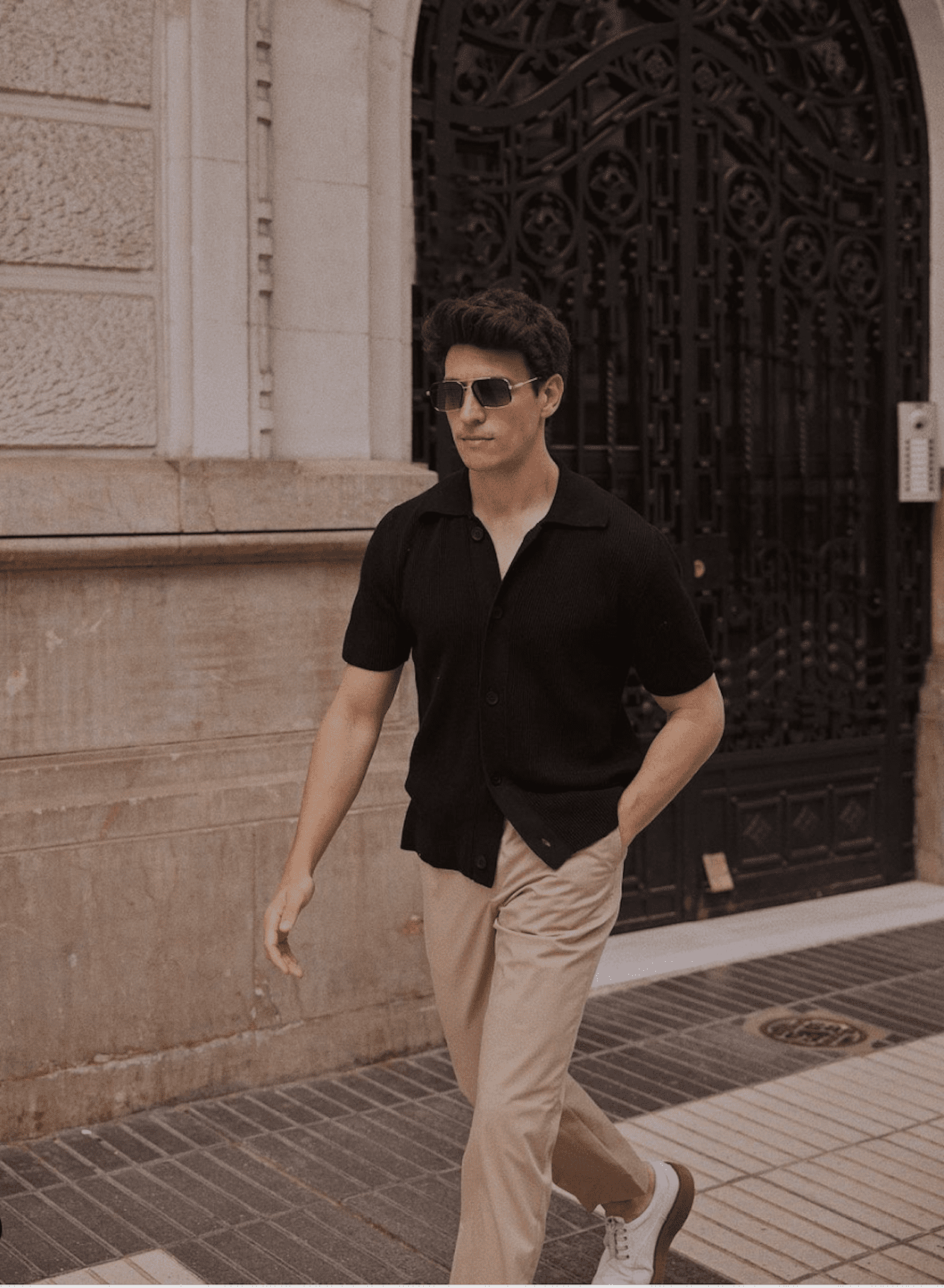 image of a man walking down the sidewalk wearing a black button up shirt, khaki pants, and white leather sneakers