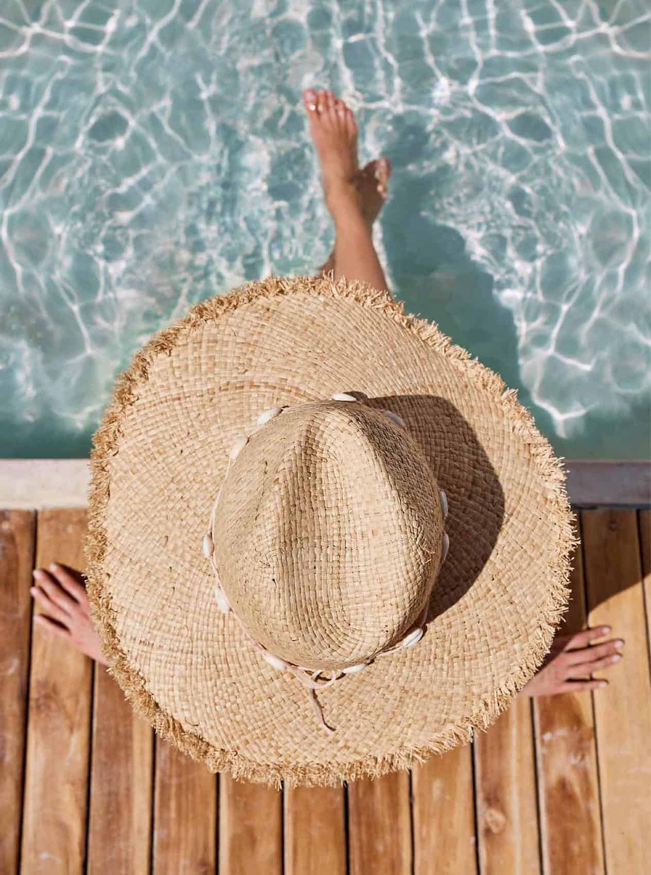 image of a woman wearing a large sun hat with her feet in a swimming pool