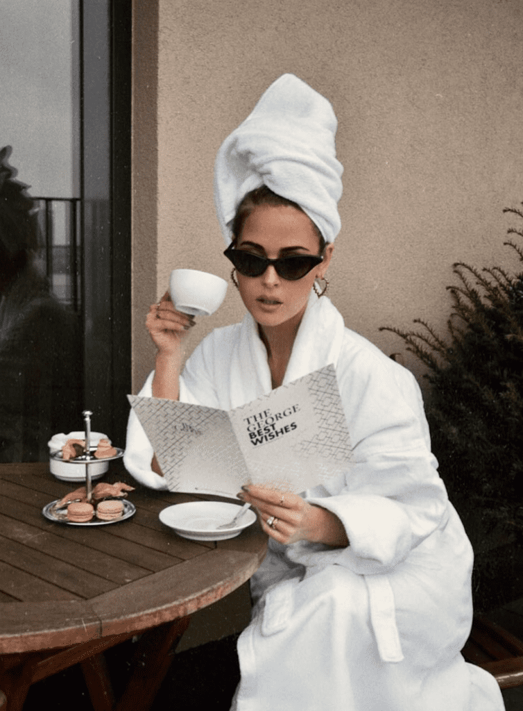 image of a woman wearing a white robe, towel on her head, sunglasses, and sitting at a table reading a menu