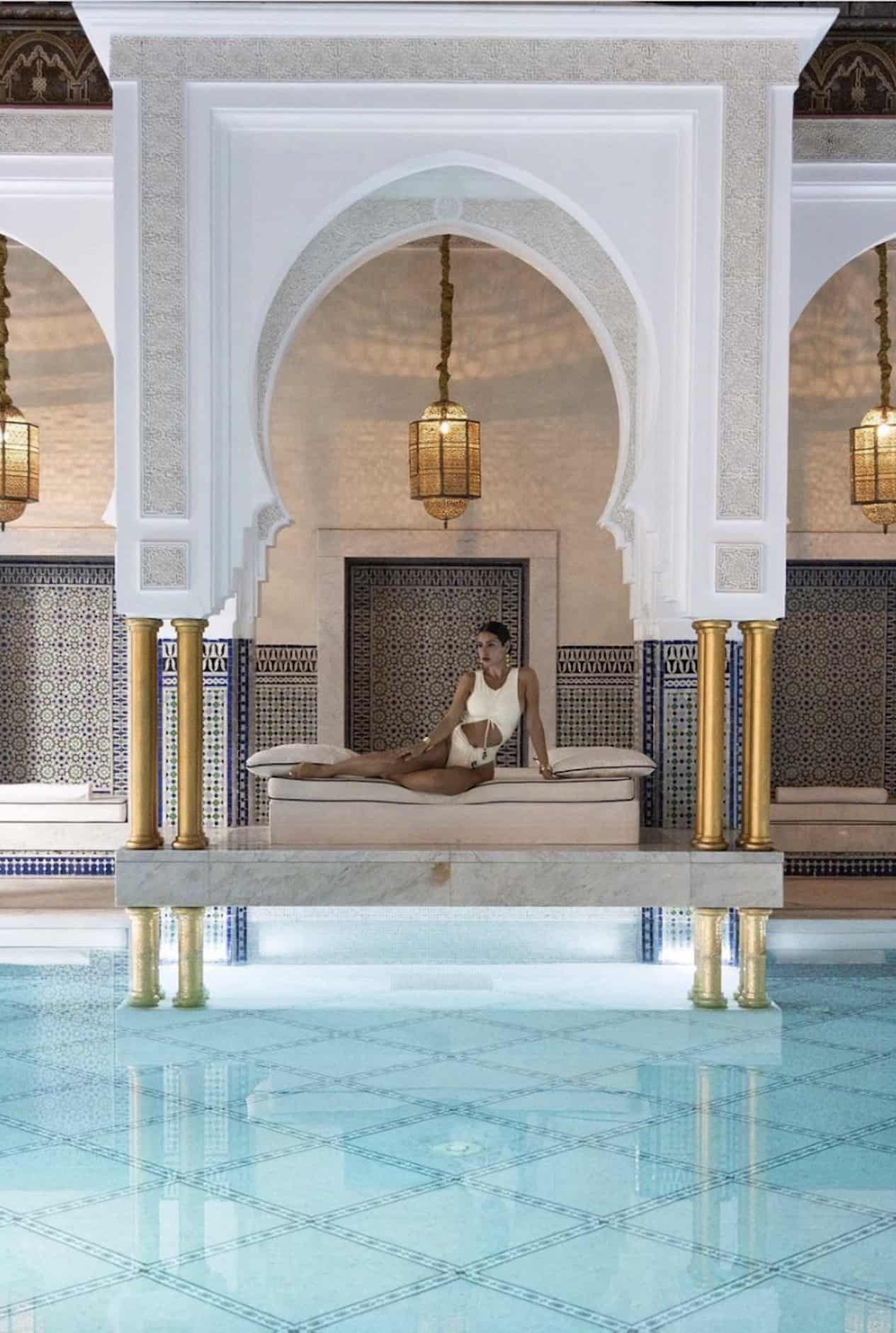 image of a woman sitting in the middle of a luxurious indoor pool at a spa, wearing a white swimsuit