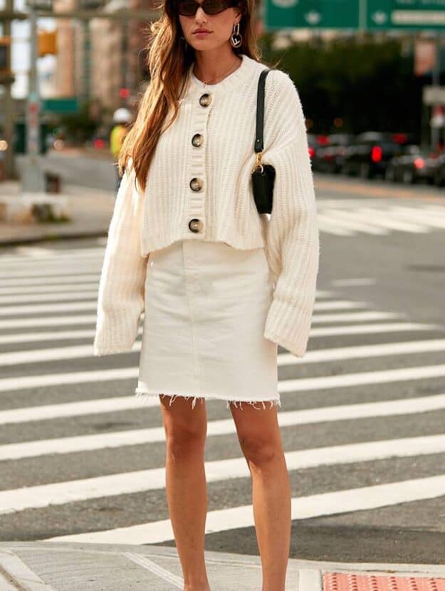 image of a woman in a white jean skirt, ivory chunky knit cardigan, and white kitten heel sandals