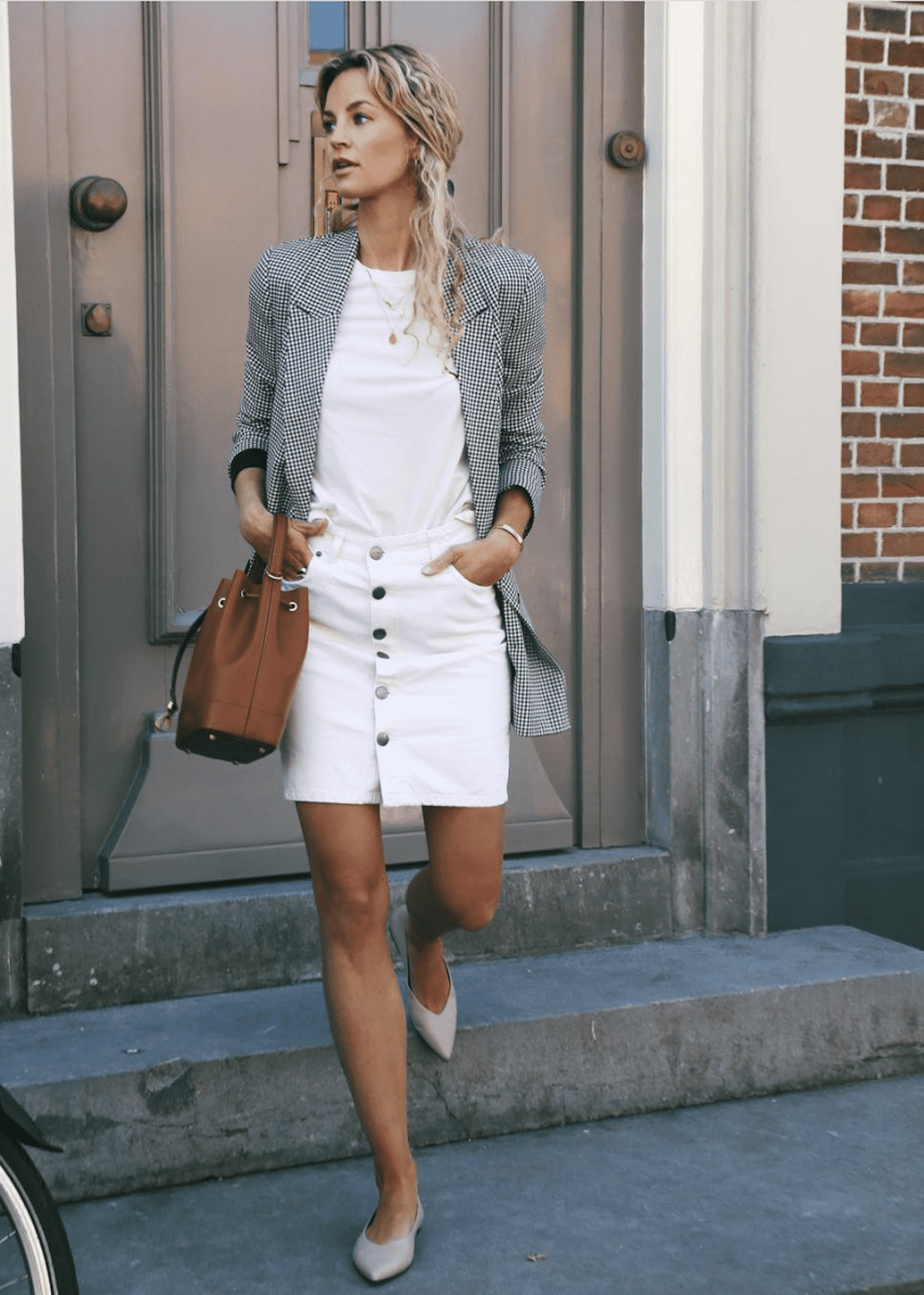 image of a woman in a white button jean skirt, white t-shirt, check blazer, and flats