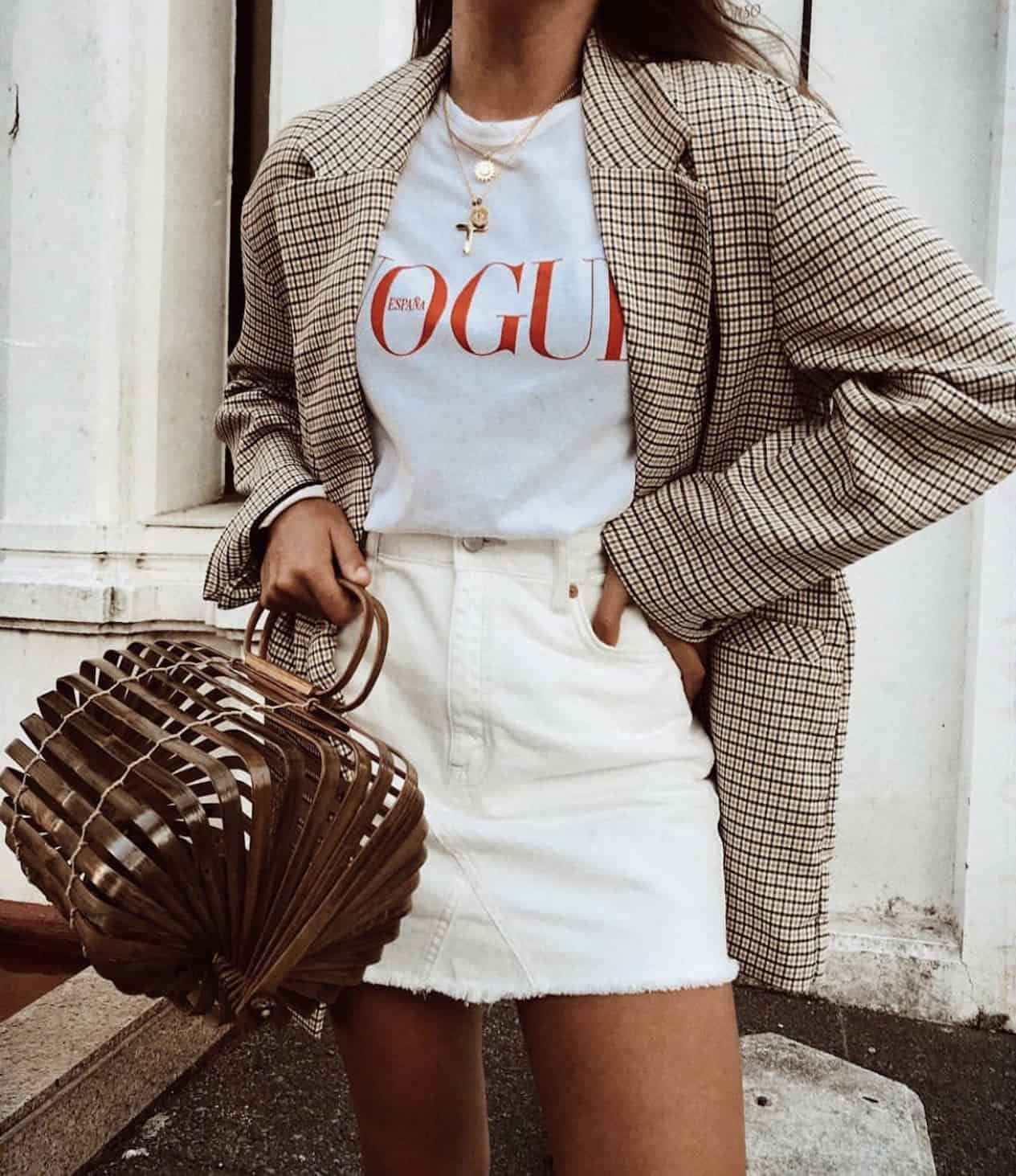image of a woman in a vogue t-shirt, plaid blazer, white jean skirt, holding a large bamboo bag
