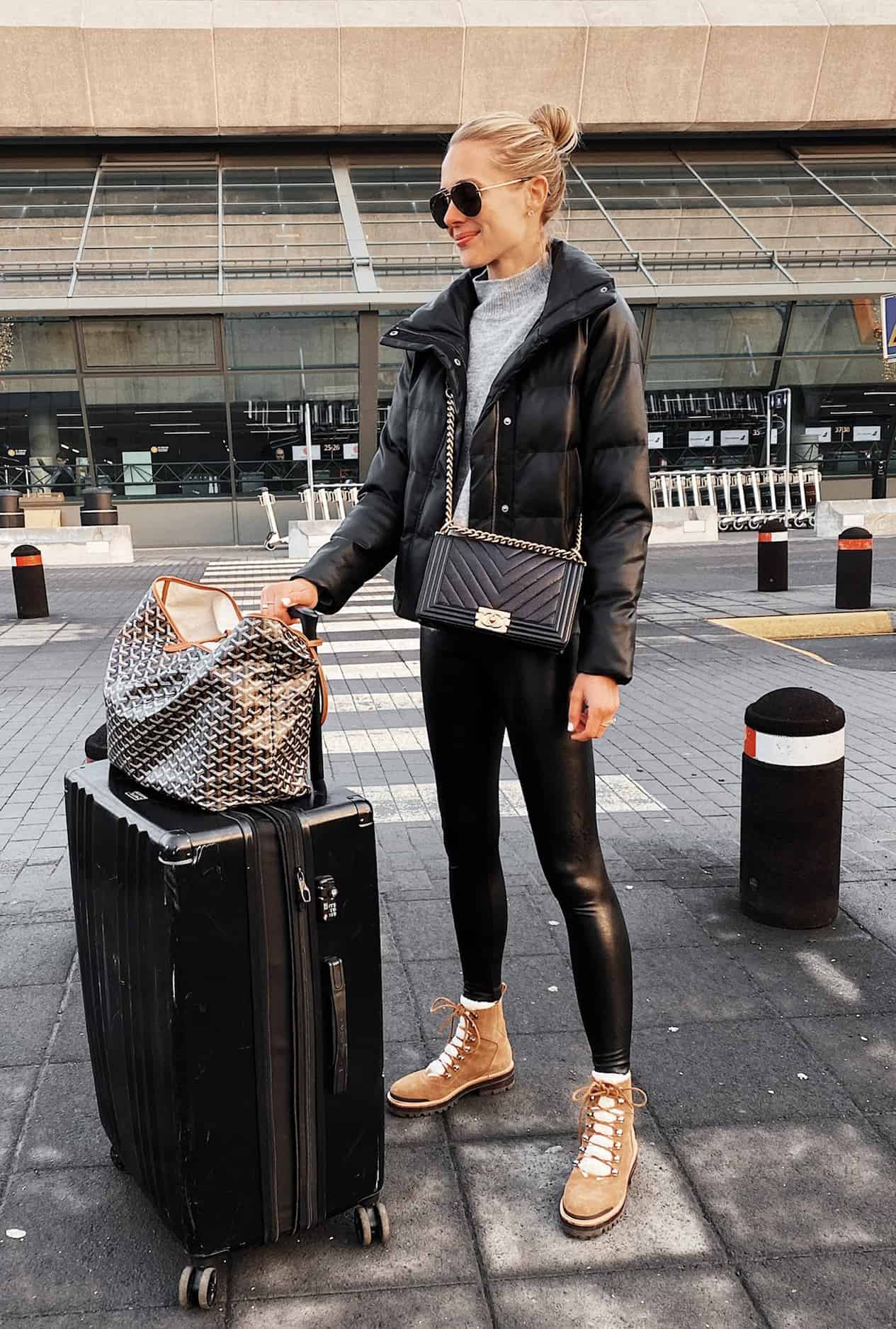 image of a woman standing in an airport terminal wearing a black puffer jacket, leather leggings, and winter boots