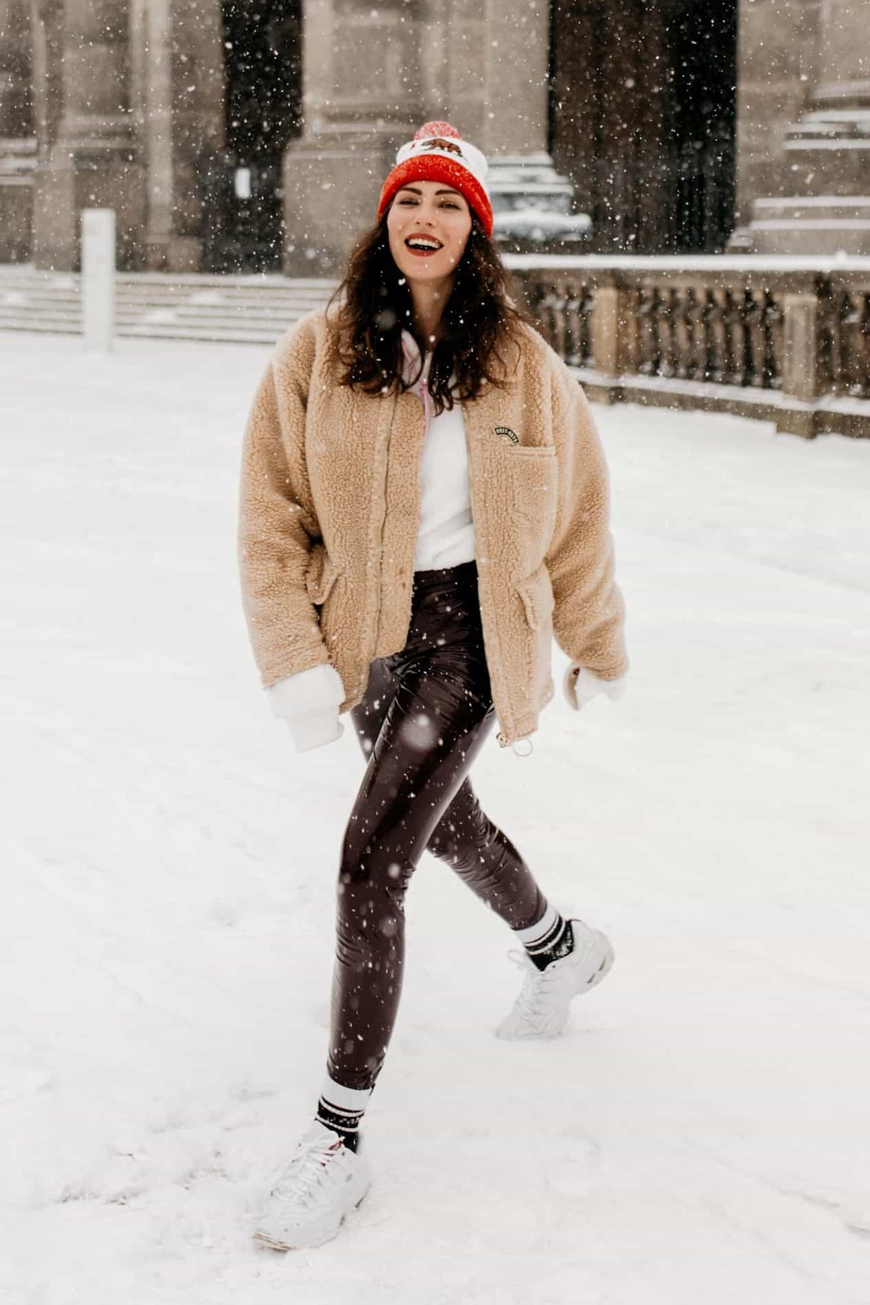 image of a woman running through the snow in a shearling jacket, leather leggings, and white sneakers