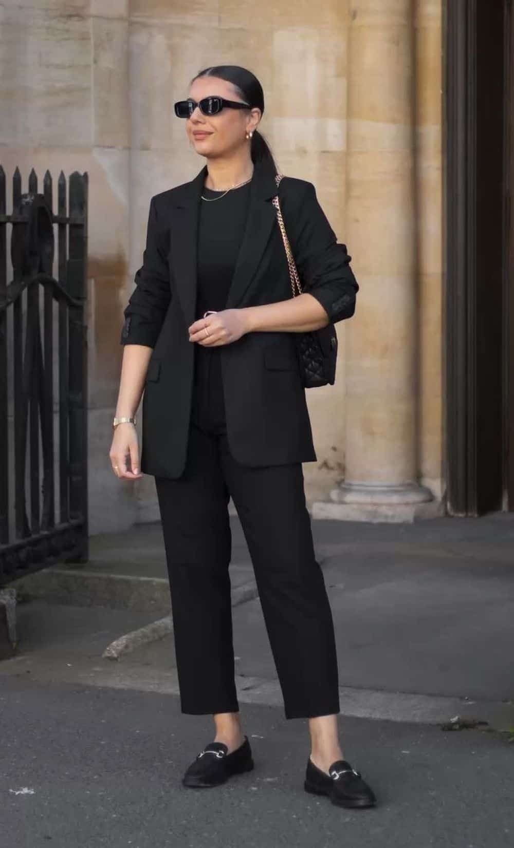 image of a woman in a black blazer, black top, black trousers, and black shoes