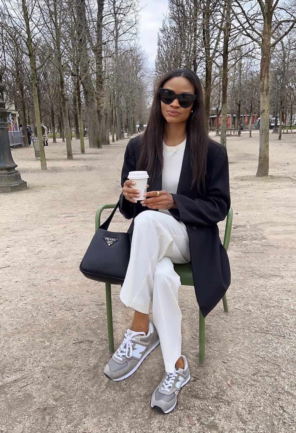image of a black woman sitting on a park bench wearing an oversized blazer, white trousers, a white shirt, and athletic sneakers
