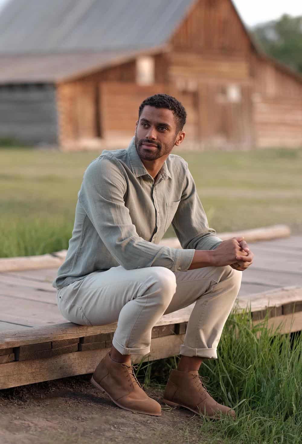 image of a man sitting outdoors wearing brown chukka boots, khaki pants, and a button up shirt