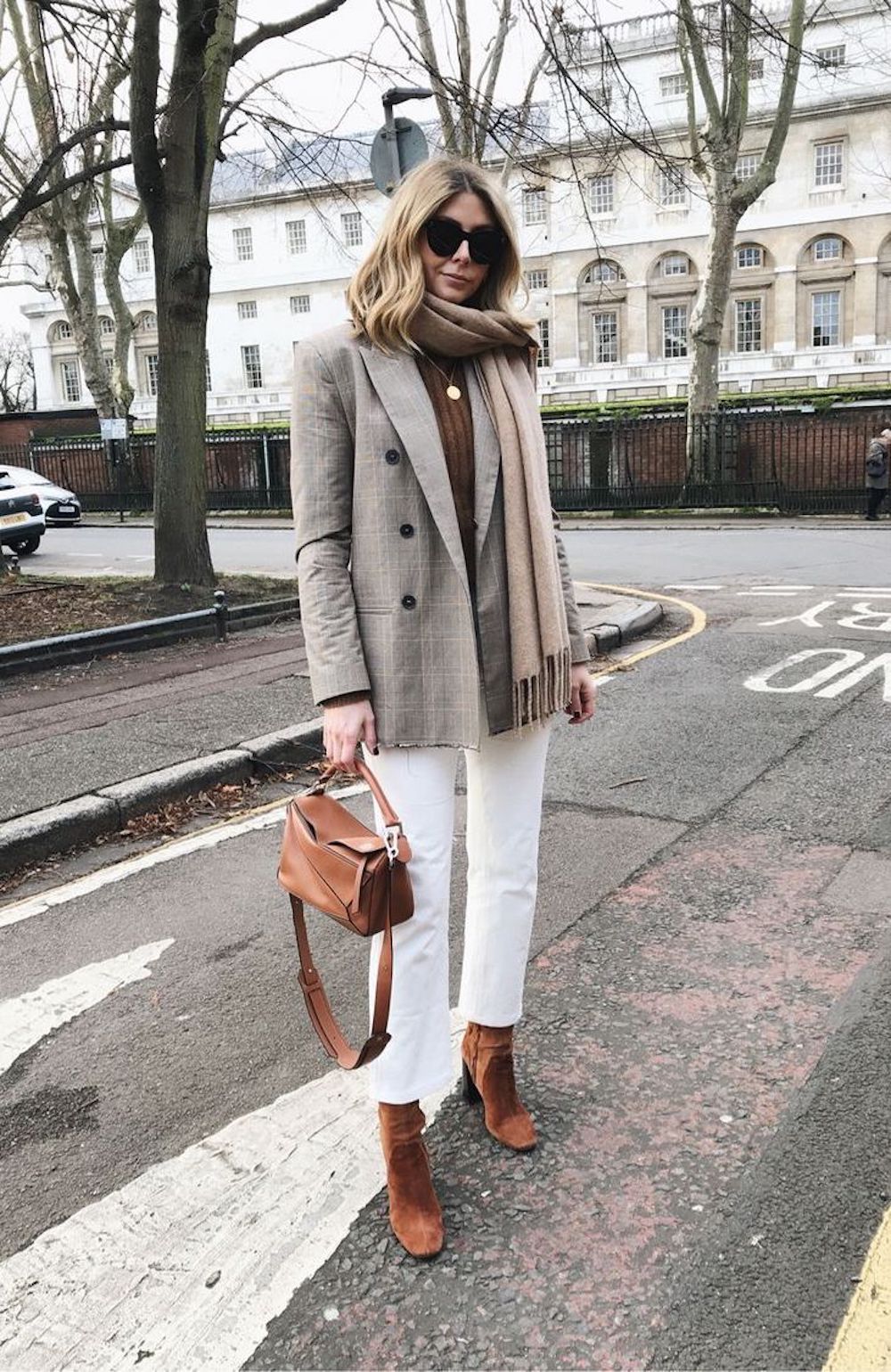 image of a woman wearing a plaid blazer, white jeans, brown boots, holding a brown purse 