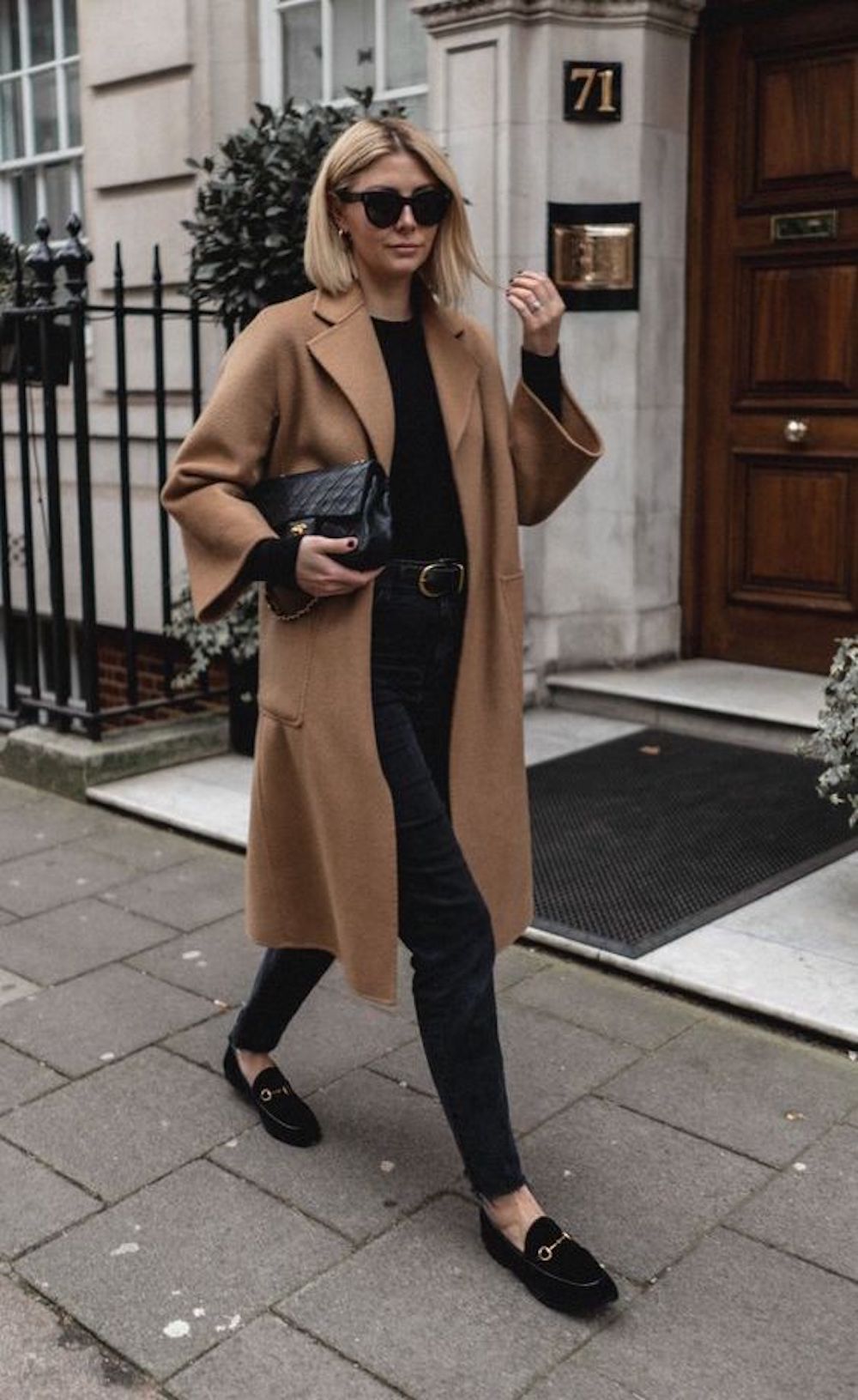 image of a woman walking down the road in a camel coat, black sweater, and black pants