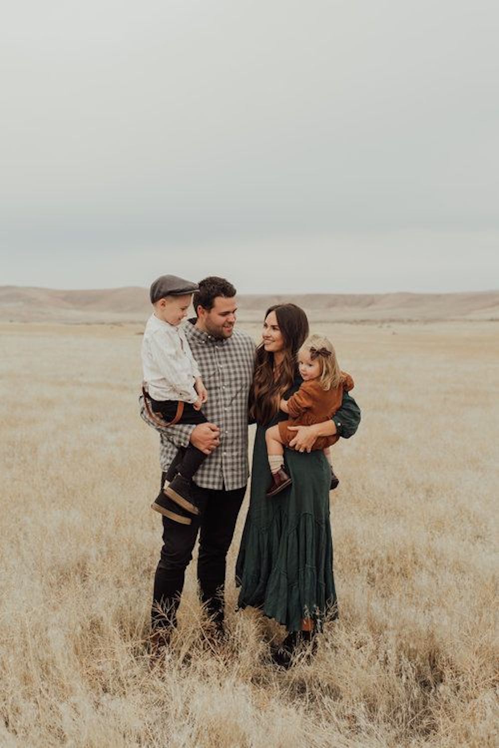 image of a family with a man, woman, and two small children standing in a wheat field wearing fall outfits for family photos