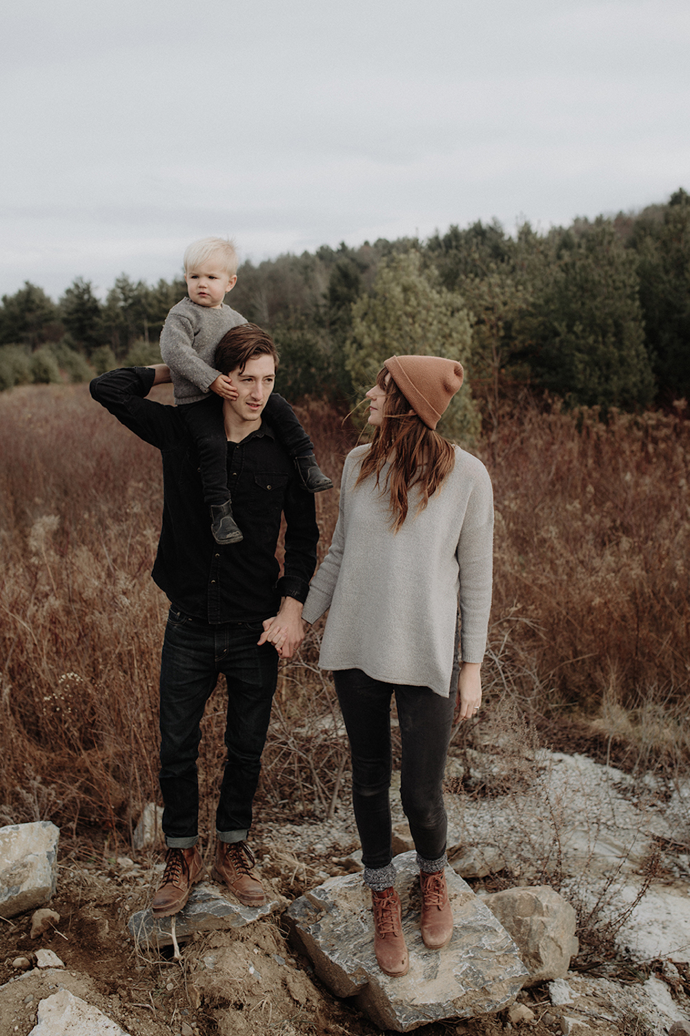 image of a family of three in the fall outdoors wearing grey knit sweaters, black pants, and lace up boots