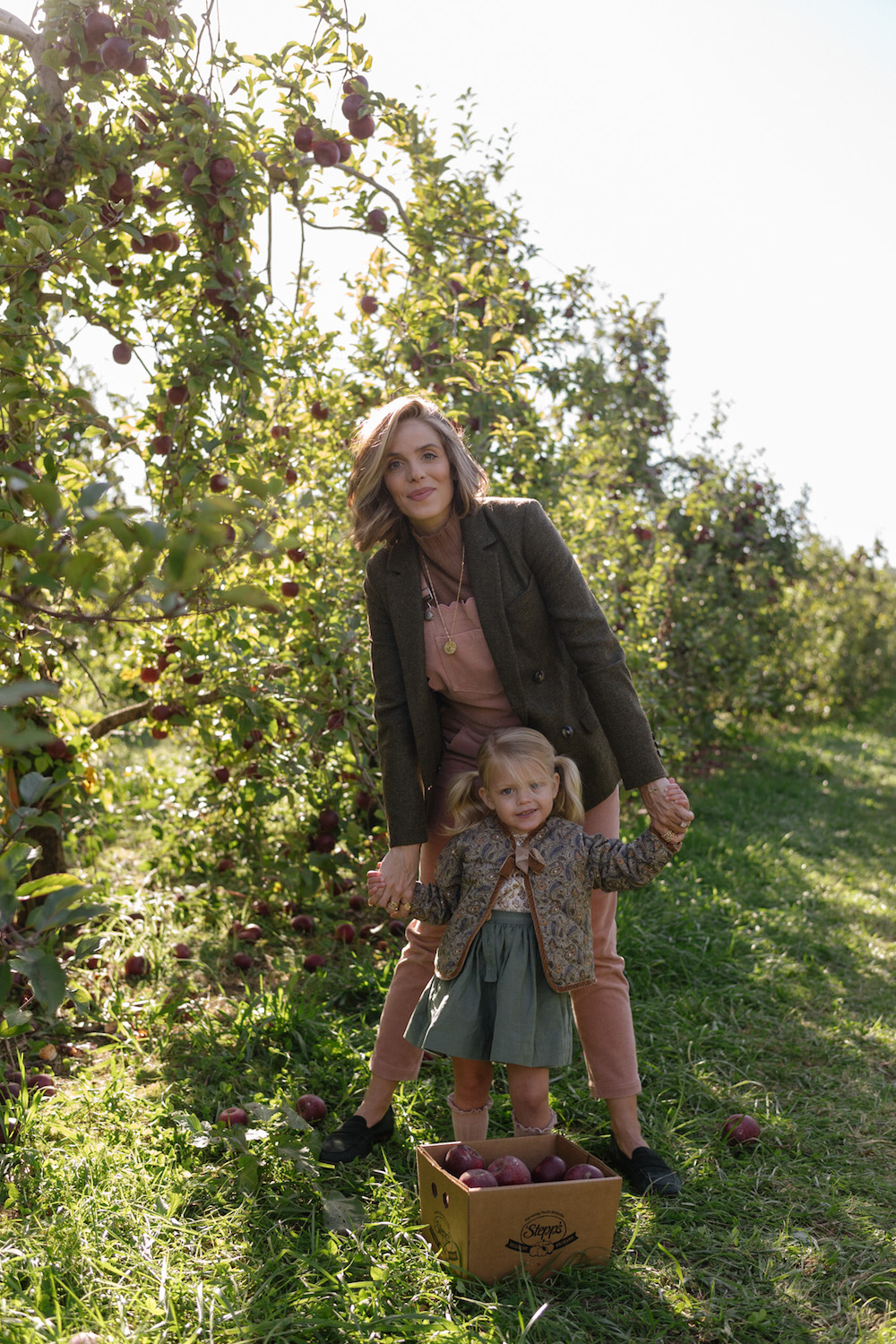 image of a mother and daughter in an apple orchard in the fall wearing neutral and dark pastel color outfits