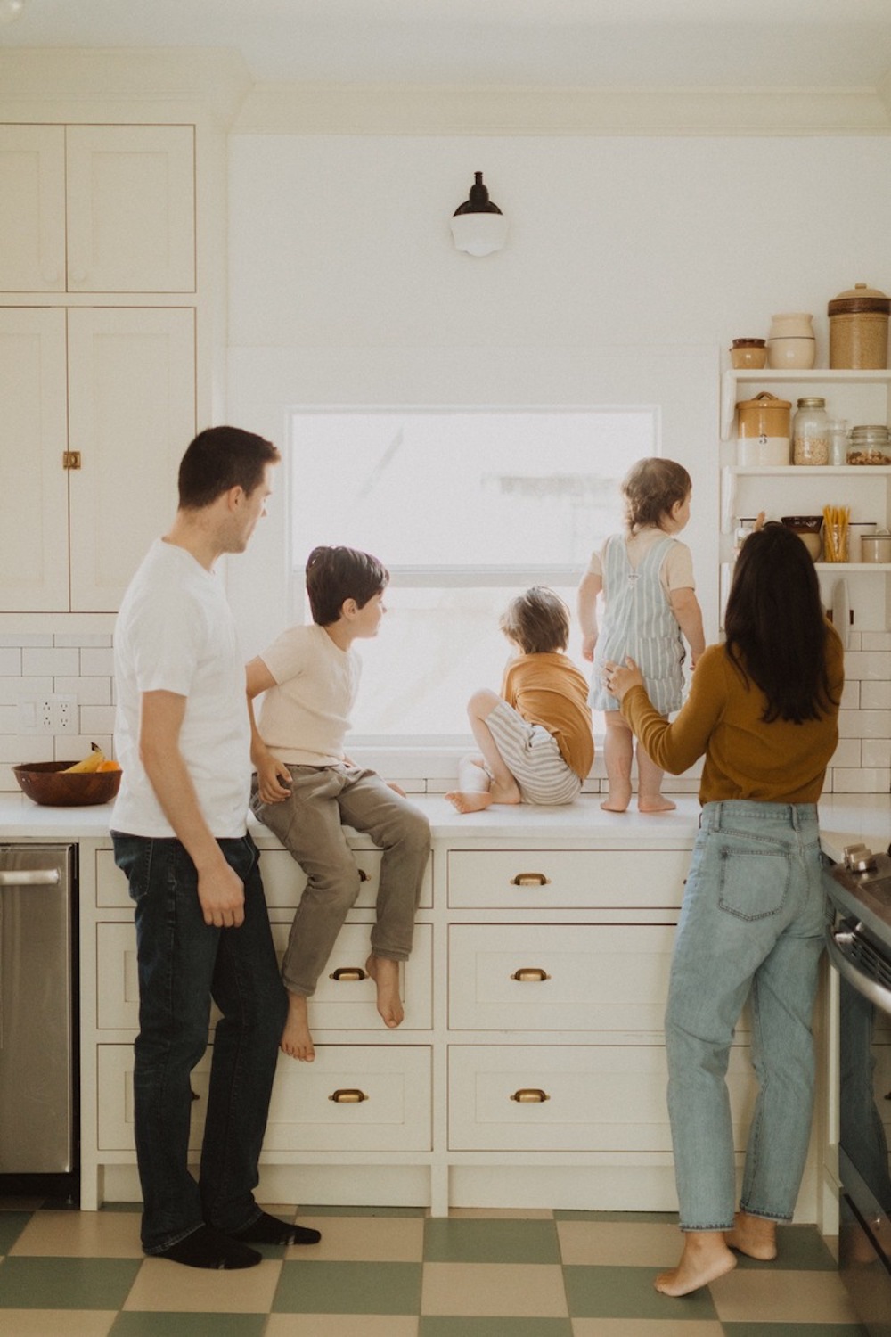 image of a family of five in a white kitchen looking out the window wearing jeans and casual neutral tops