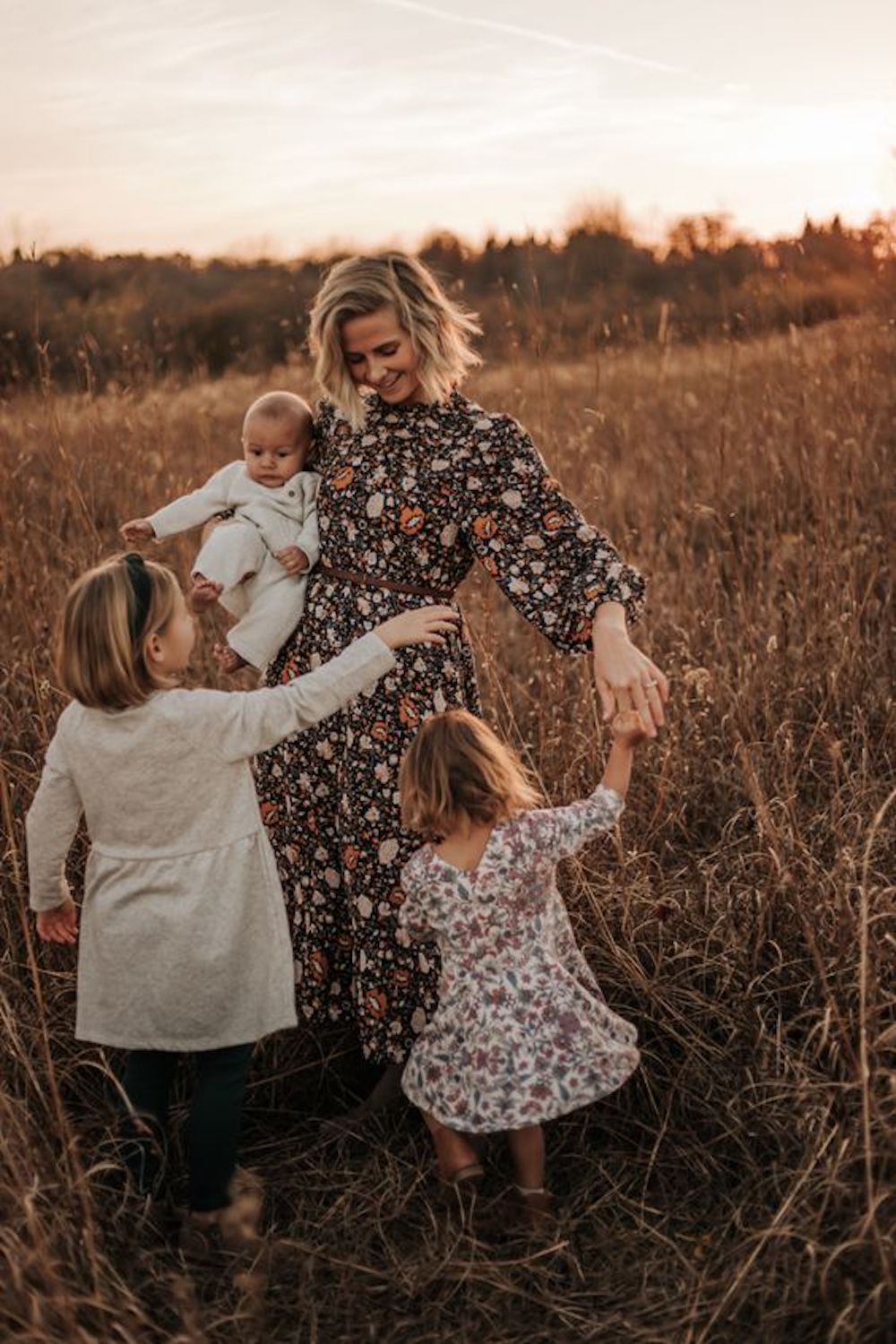 image of a mom in a black floral maxi dress twirling with three daughters in a grassy field in the fall