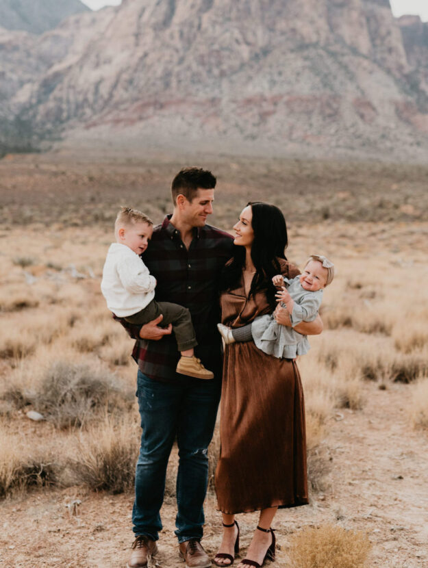 image of a family with a man, woman, and two small children in a grassy field wearing brown, black, and ivory clothing