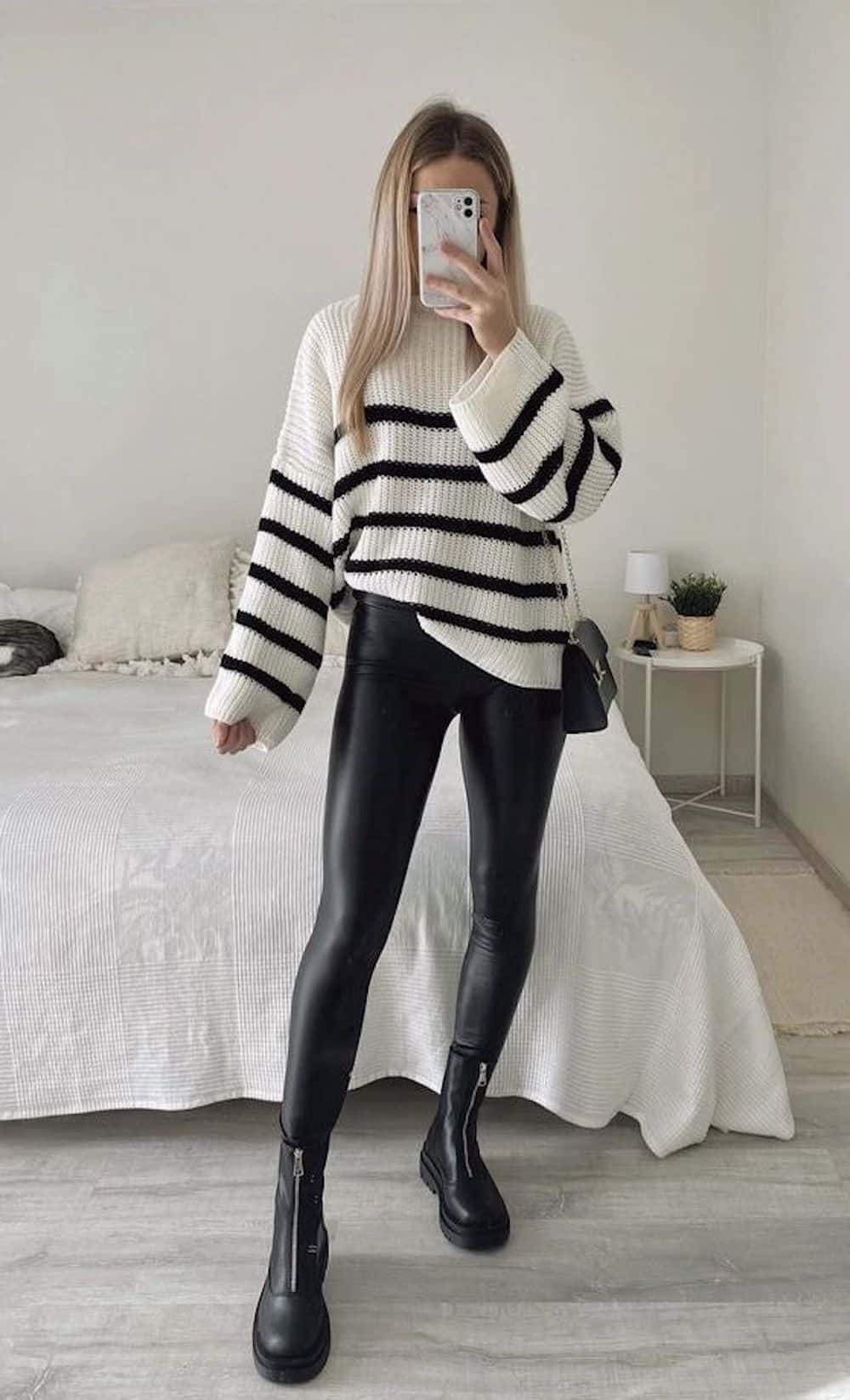 image of a woman in an oversized striped knit sweater, black faux leather leggings, and black lug boots