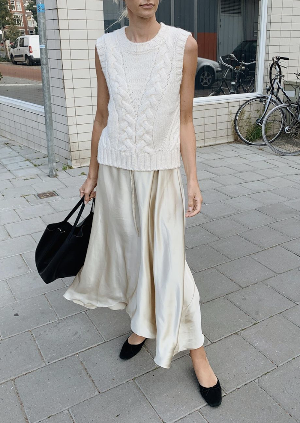 image of a woman in a sweater vest over a maxi slip dress in ivory with black shoes