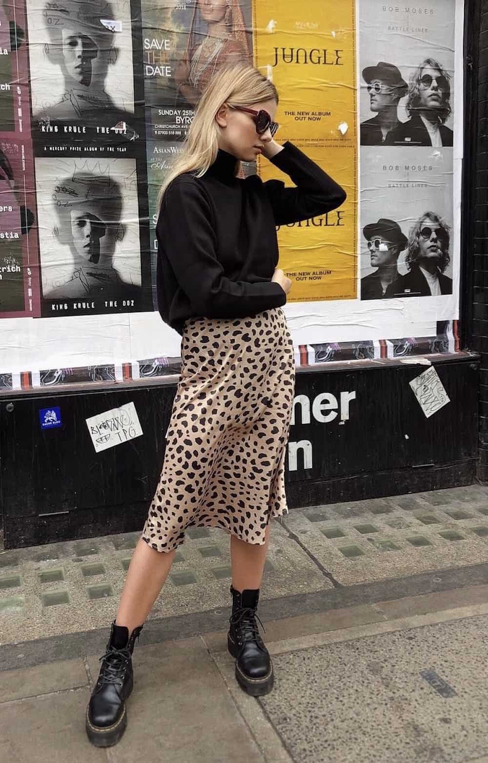 image of a woman wearing a black knit sweater, a leopard print midi skirt, and black lug boots