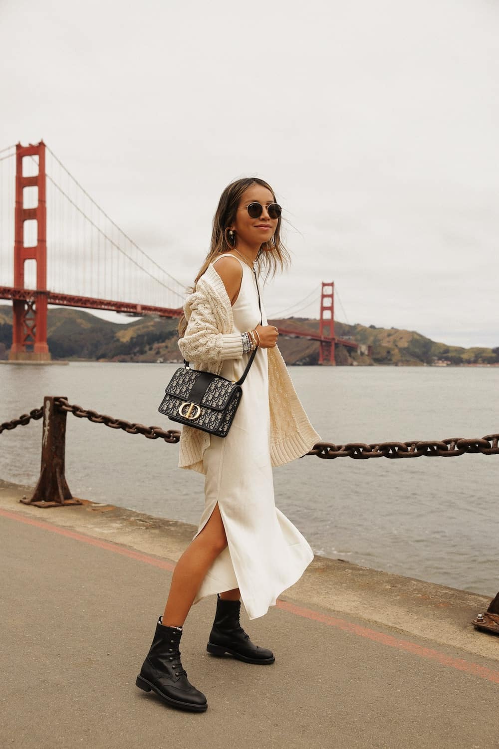 image of a woman in a white midi slip dress, a beige cardigan, and black combat boots in front of the Golden Gate bridge
