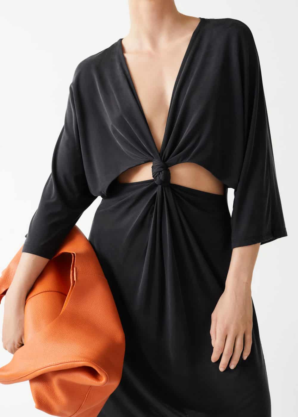 image of a woman in a black cutout dress holding an orange leather bag