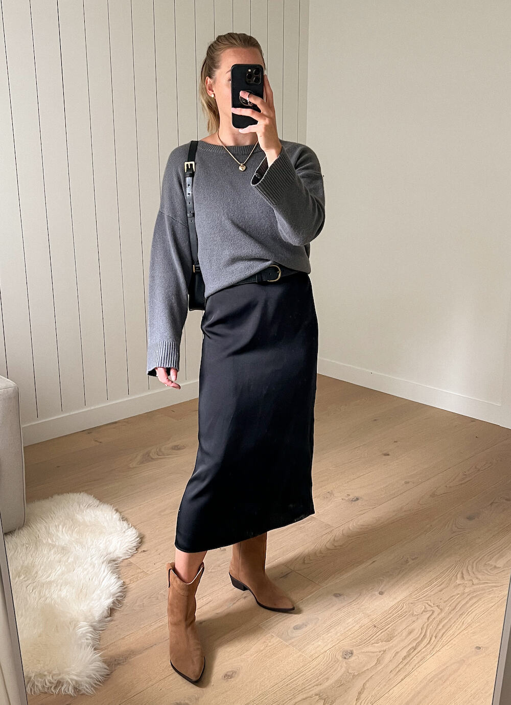 woman wearing a grey cashmere sweater over a a long black slip dress with brown suede western style boots 