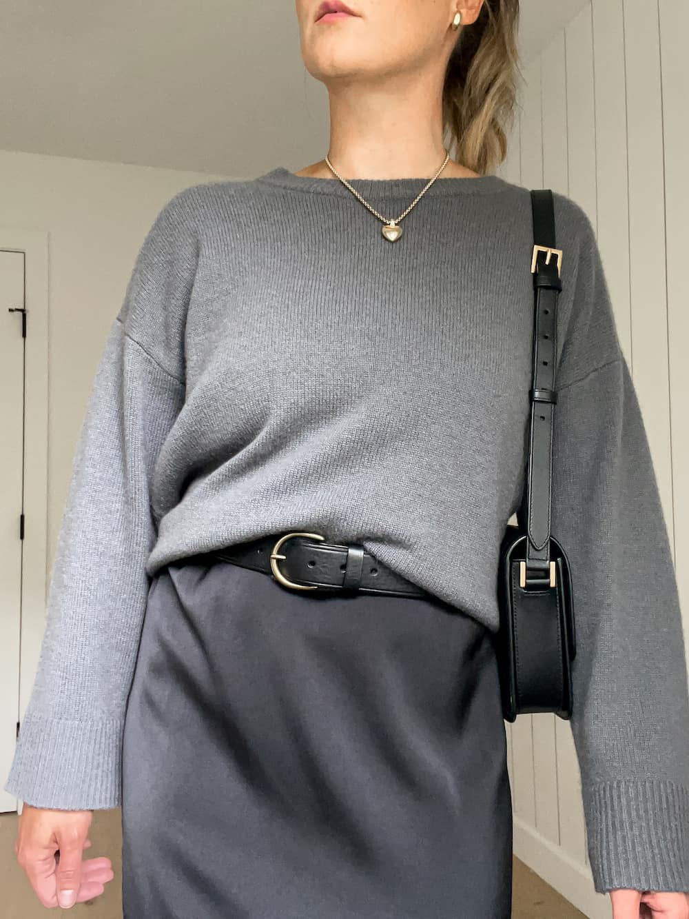 woman wearing a cashmere sweater over a black slip dress with a black leather belt 