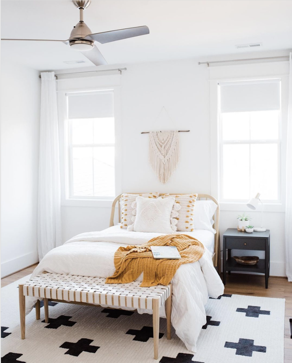 image of a white bedroom with a rattan bed, wooden bench, and black nightstand 