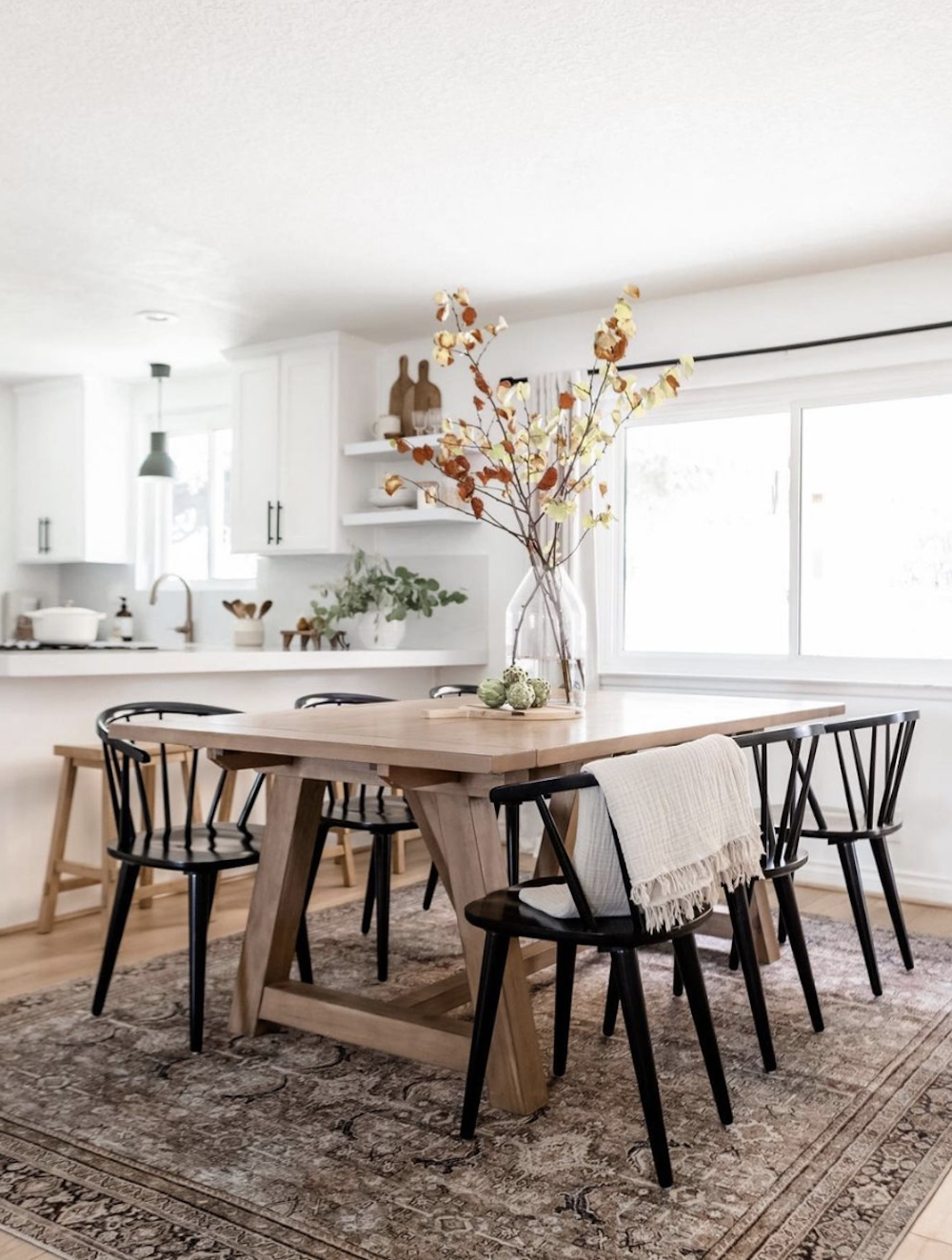 image of a white kitchen and dining area with a wood table and black spindle chairs