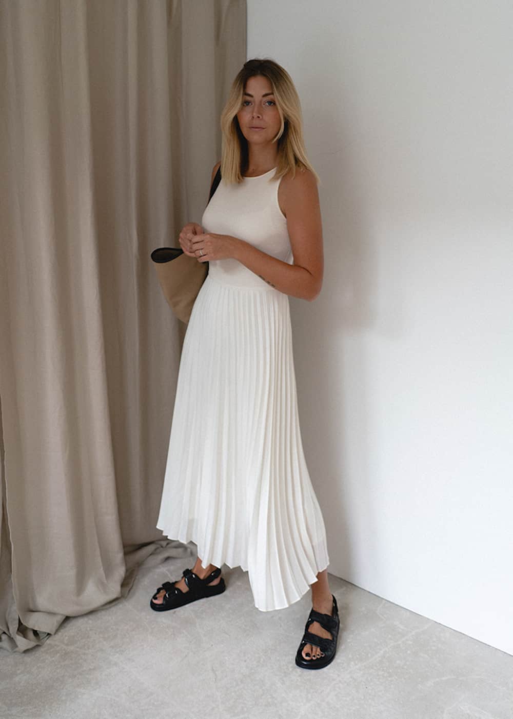 image of a woman in a pleated white tank dress and black chunky sandals